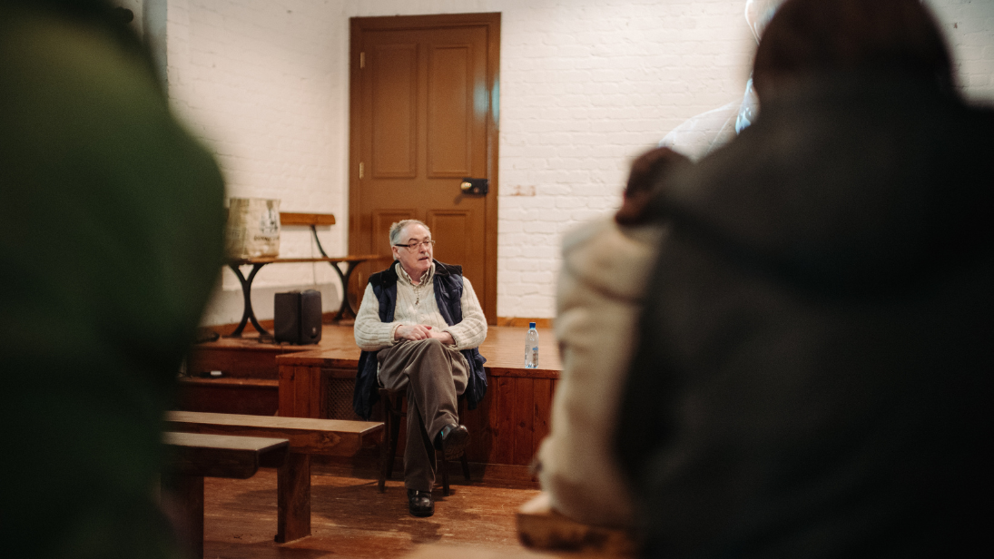 Dr Maurice Casey sitting on stage during a talk at Ulster Folk Museum