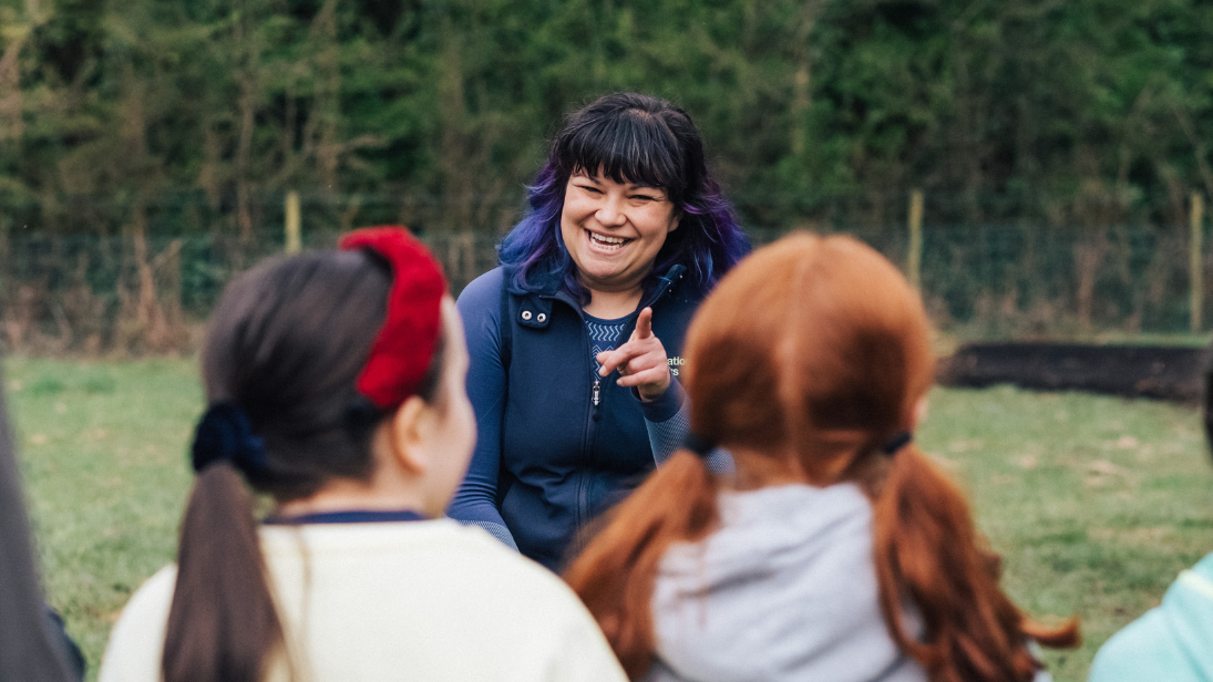 A lady with black hair speaking to two young girls with brown and red hair