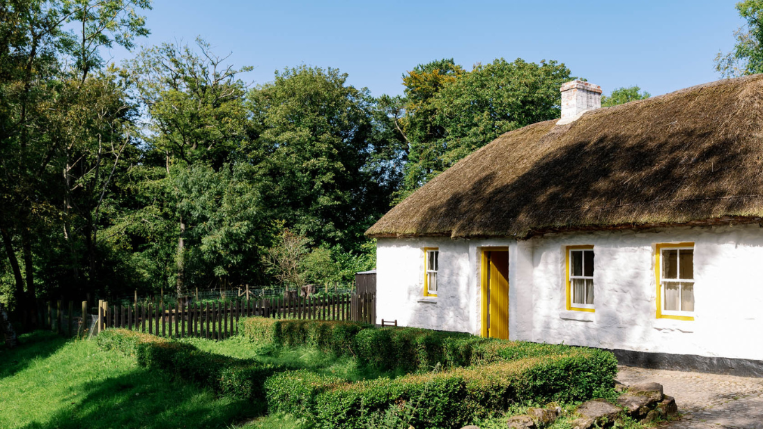 A thatched white cottage with yellow doors and windows and a large garden. 