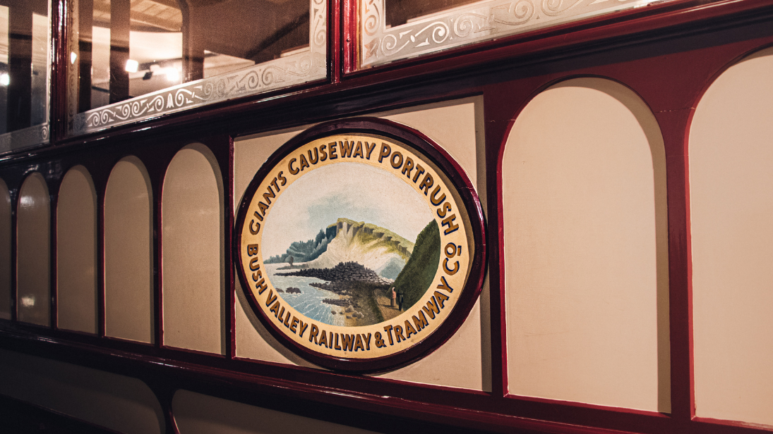 The side of an old tram with a logo reading 'Giants Causeway Portrush Bush Valley Railway & Tramway Co'. 