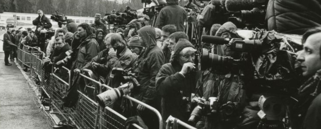 Black and white photograph of press behind a fence, during the signing of the Good Friday Agreement