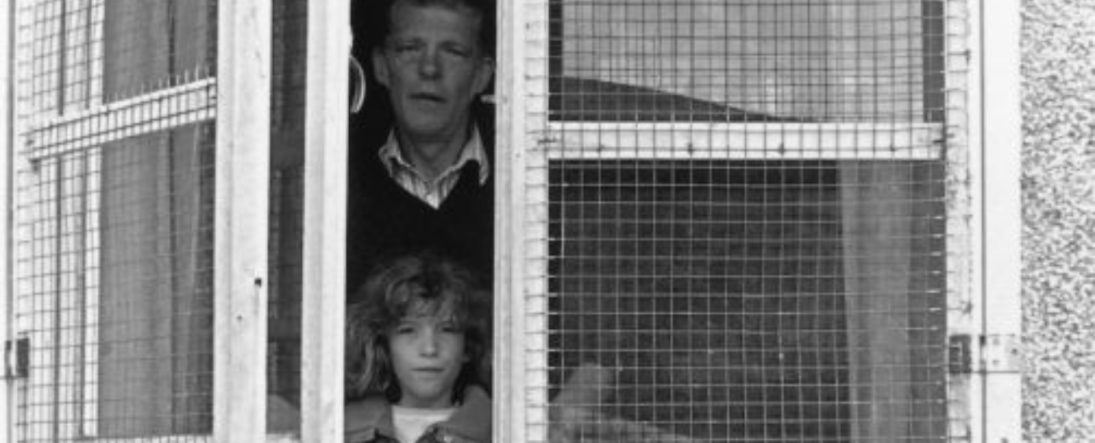 Black and white photograph of a man and young girl looking out of a caged up window