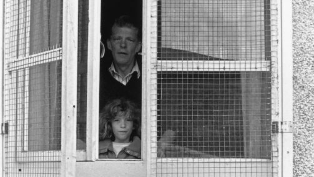 Black and white photograph of a man and young girl looking out of a caged up window