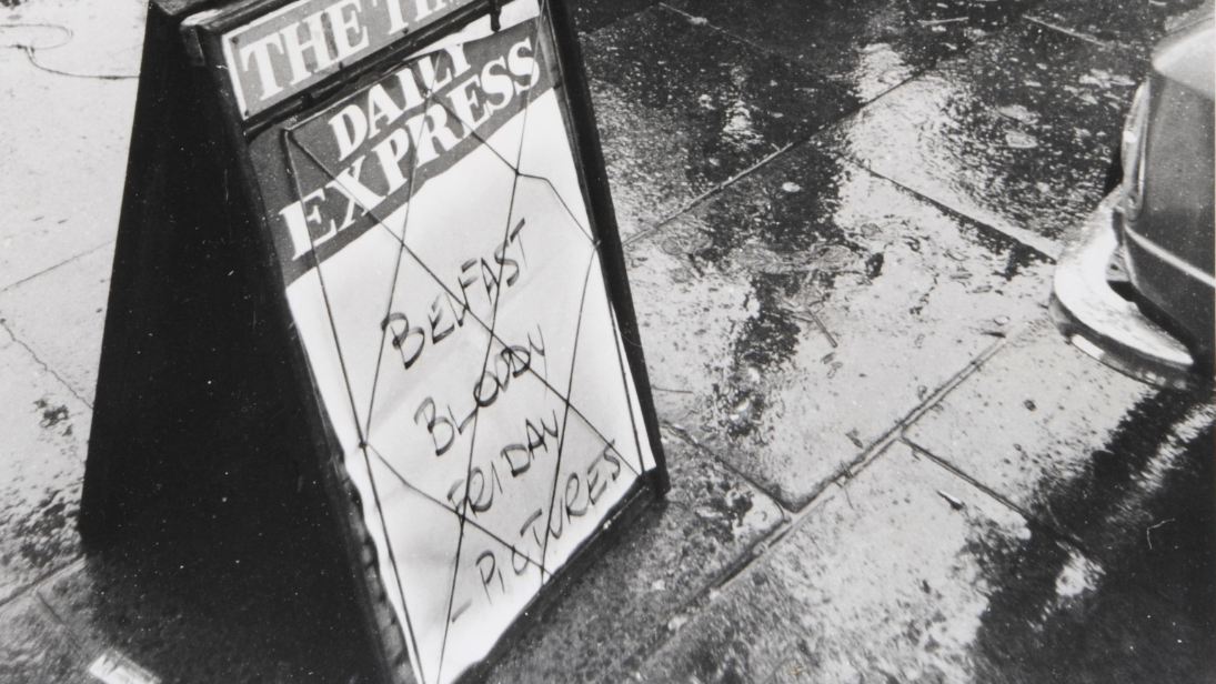 Black and White photograph of sandwich board which says 'Belfast Bloody Friday Pictures'