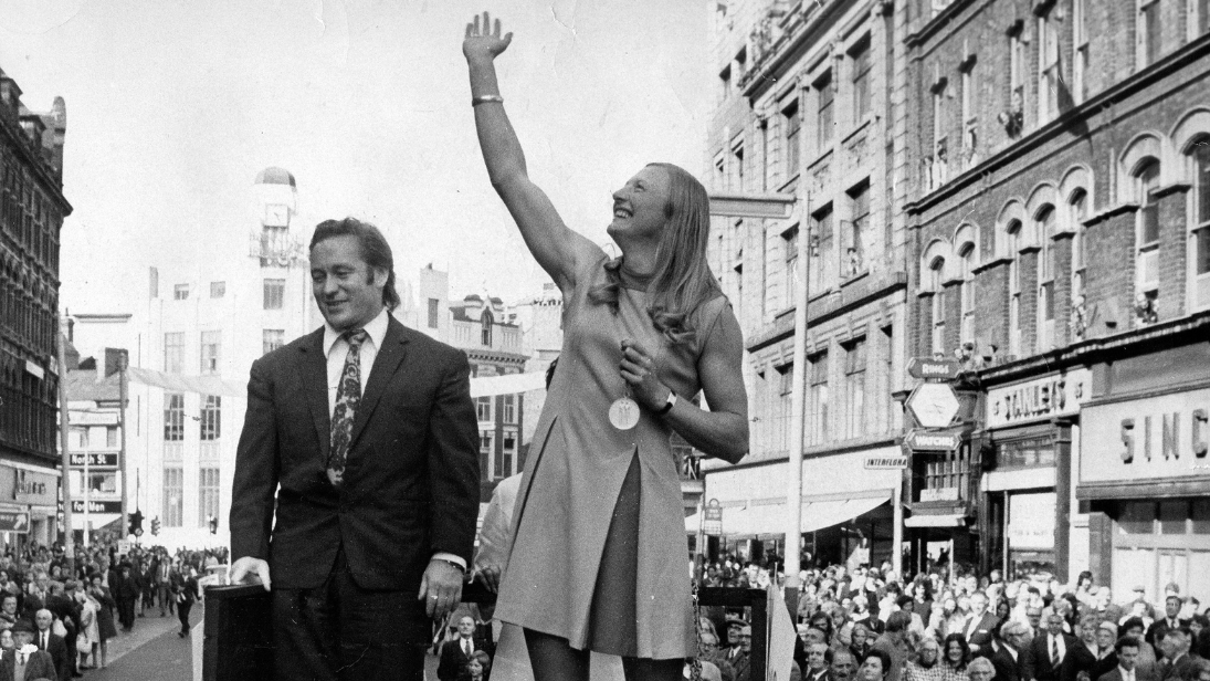 Black and white photograph of Mary Peters holding her gold olympic medal waving