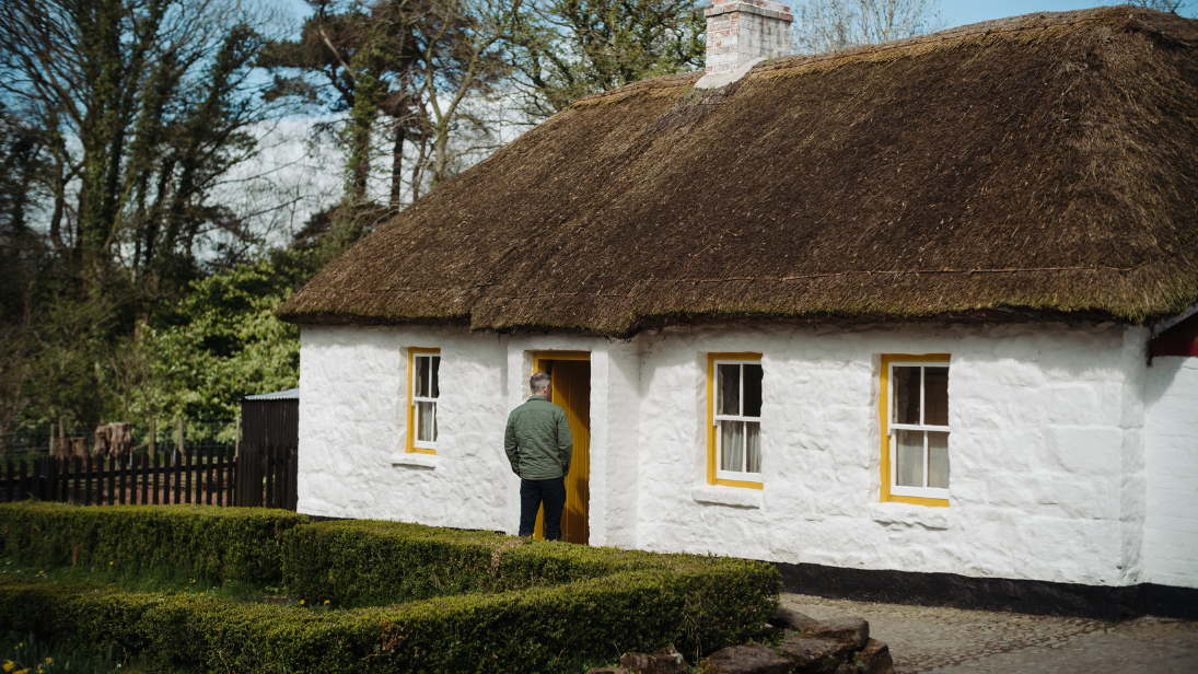 A man walking into Coradreenan Farmhouse at the ulster folk museum, a thatched white cottage with yellow windowsills