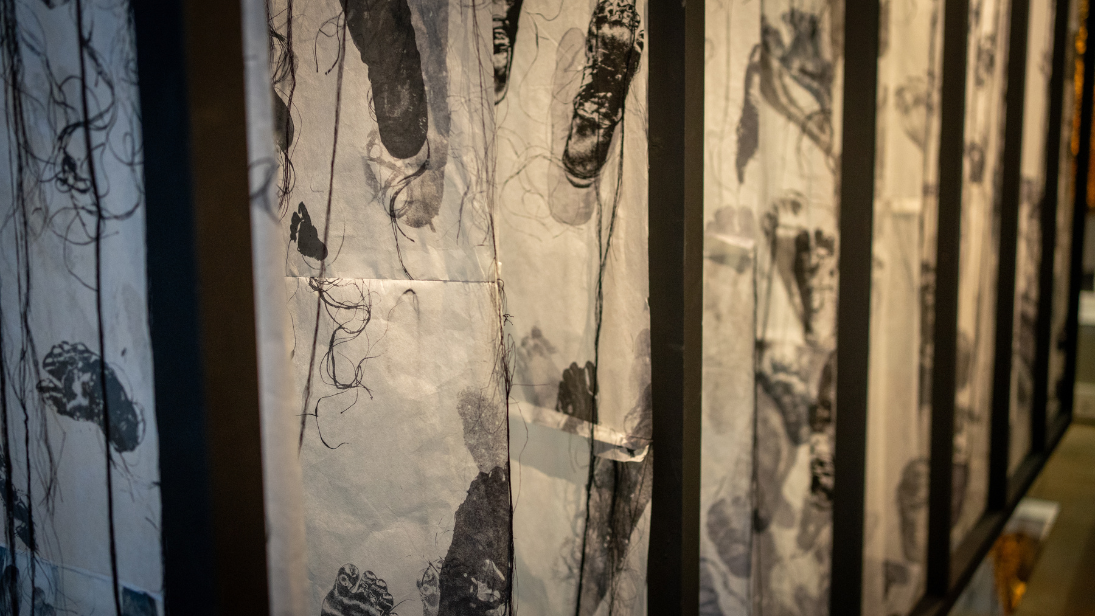 Image of installation in the window on our world gallery with black ink footprints on suspended fabric between black beams