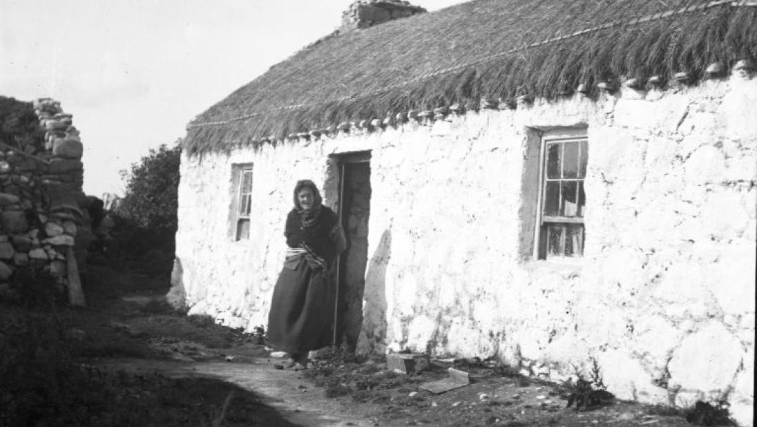 Shawled woman at doorway of rope thatched house, black and white photograph