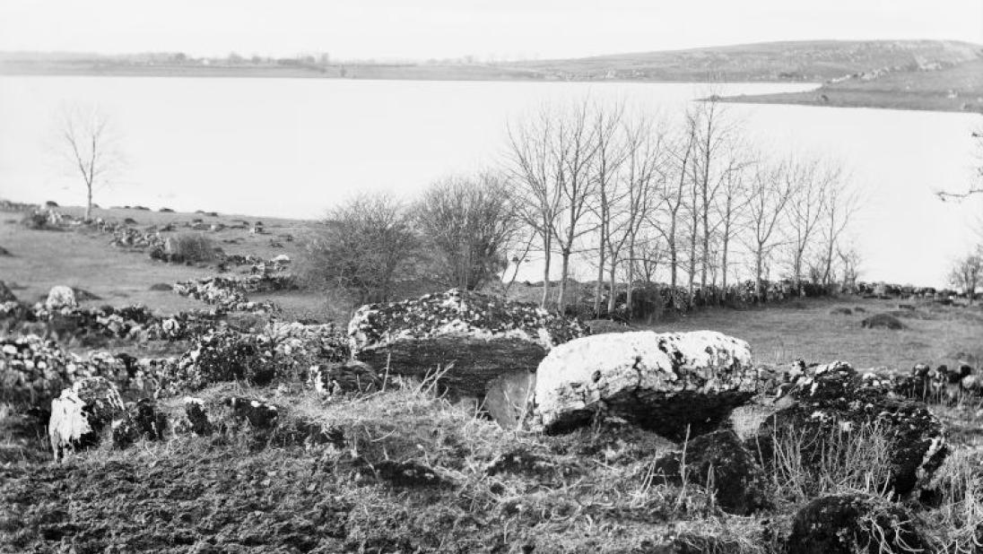 An archaeological monument sits on a hillside beside a lough.