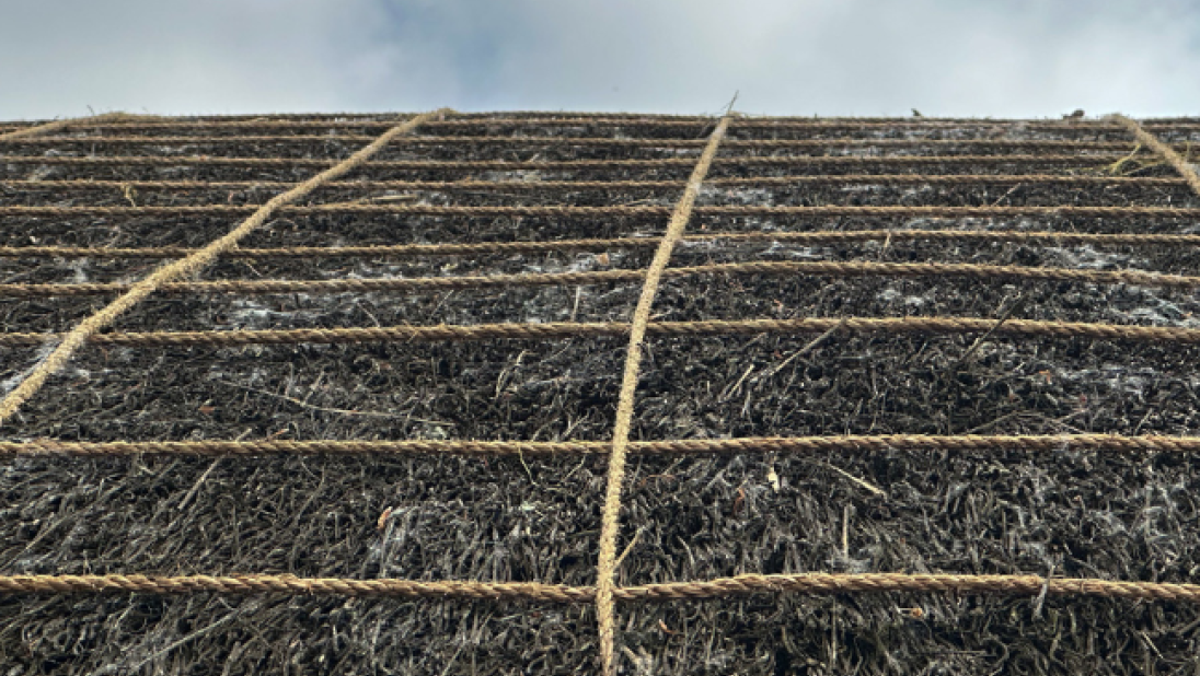 The roof of a building showing ropes holding down thatch. The ropes lie both horizonally and vertically.