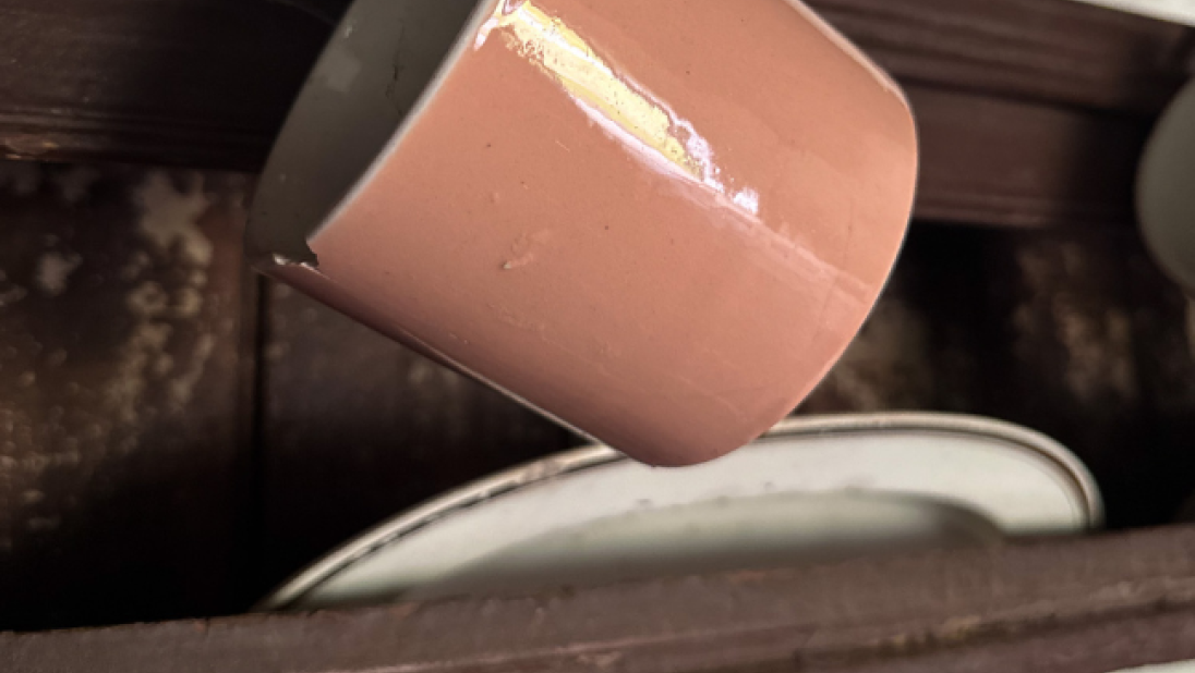 A close up of a pinkish mug hanging on a dresser. The mug has a chip in it.