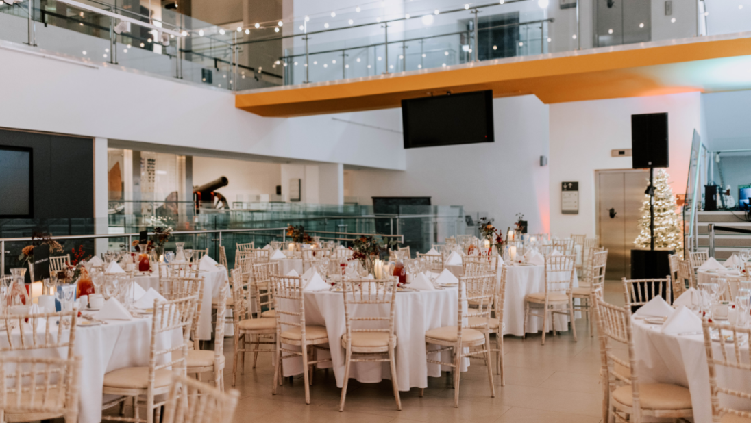 Tables and chairs set up for an event in the Ulster Museum, with festoon lights above.