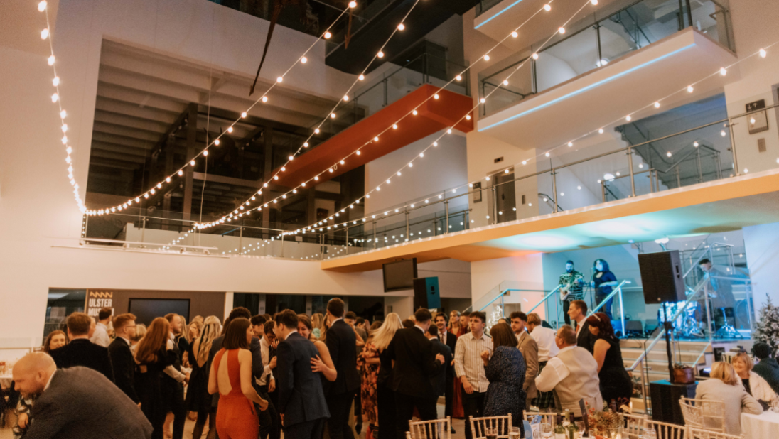 A dancefloor packed with festive party goers at the Ulster Museum, singers on steps and festoon lights hang above the dancefloor