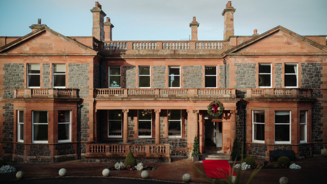 A picture of the outside of Cultra Manor with a red carpet at the front entrance and large Christmas wreath over the door