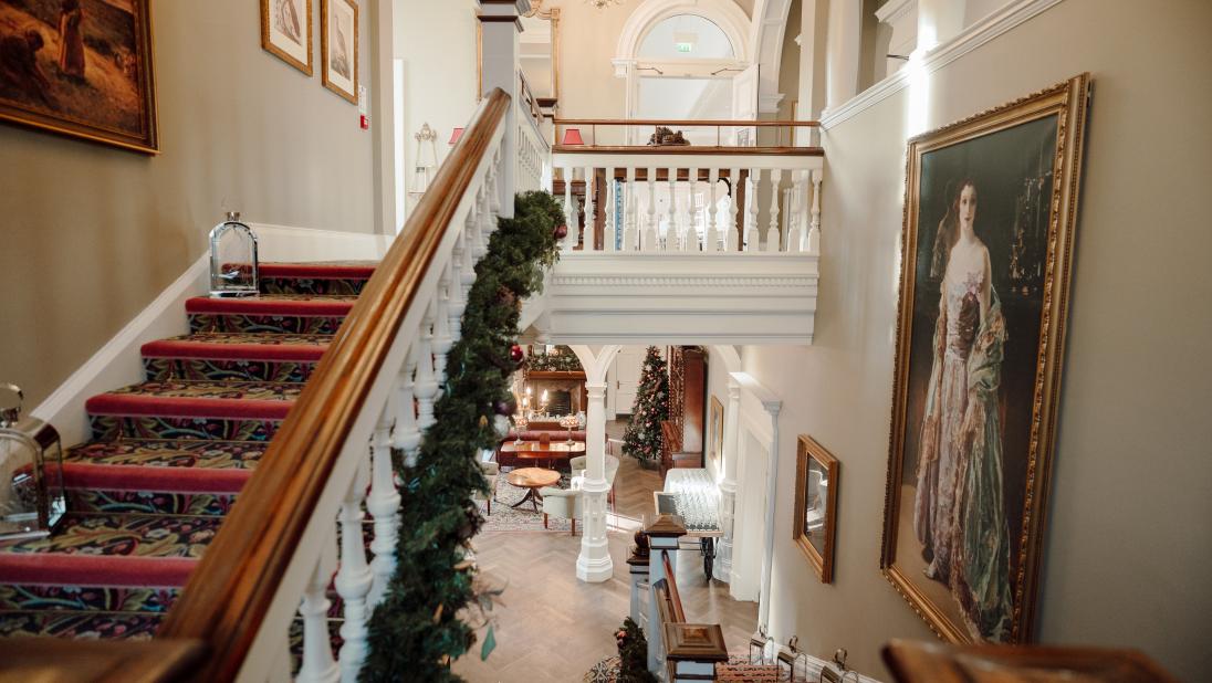 A Christmas garland added to the staircase in Cultra Manor. Grand, portrait paintings hang on the walls.