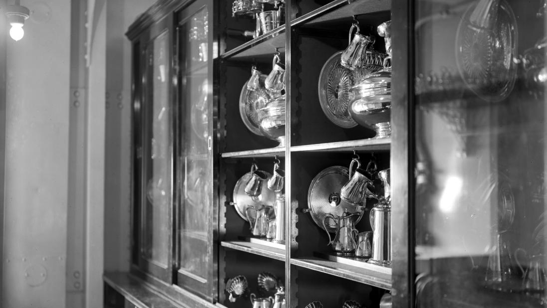A black and white image of a cabinet filled with glass dinner ware. 