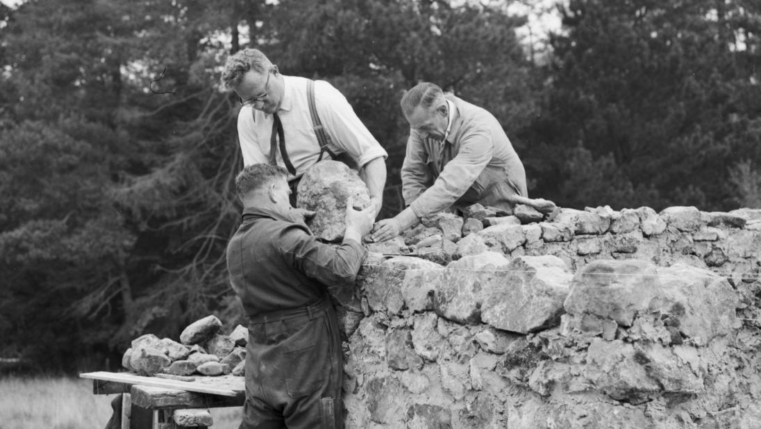 Three men are rebuilding a stone wall of a house.