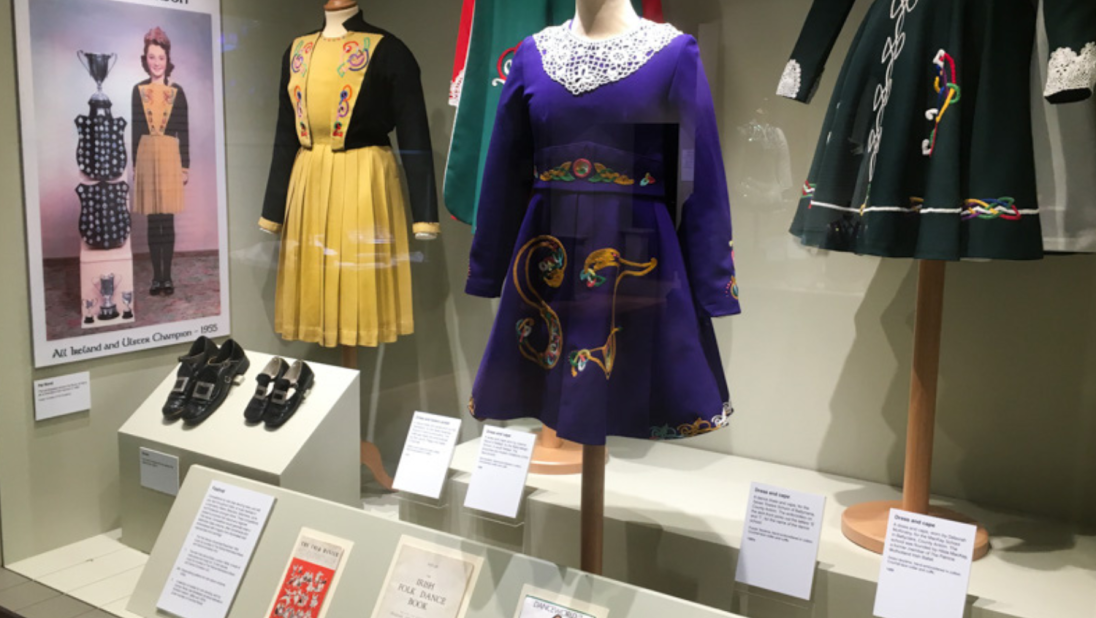 A shot of an exhibition with one yellow, one purple, and one green Irish dancing dress.