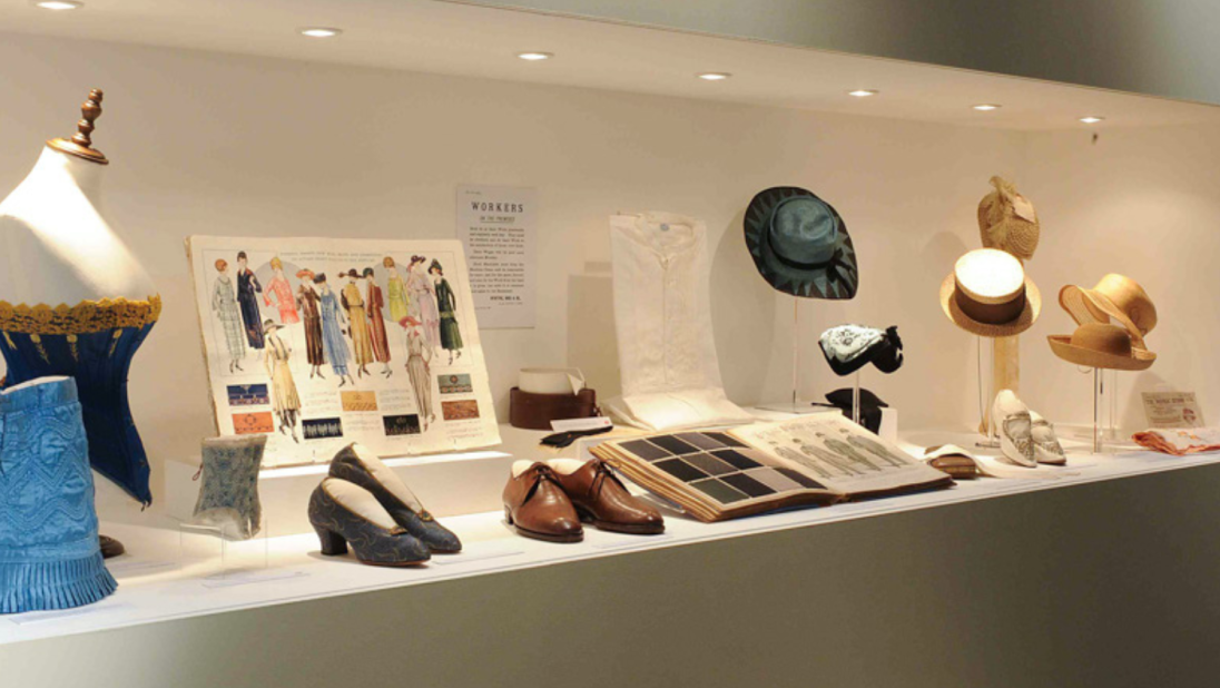 A shot of an exhibition with a corset, some shoes, and hats.