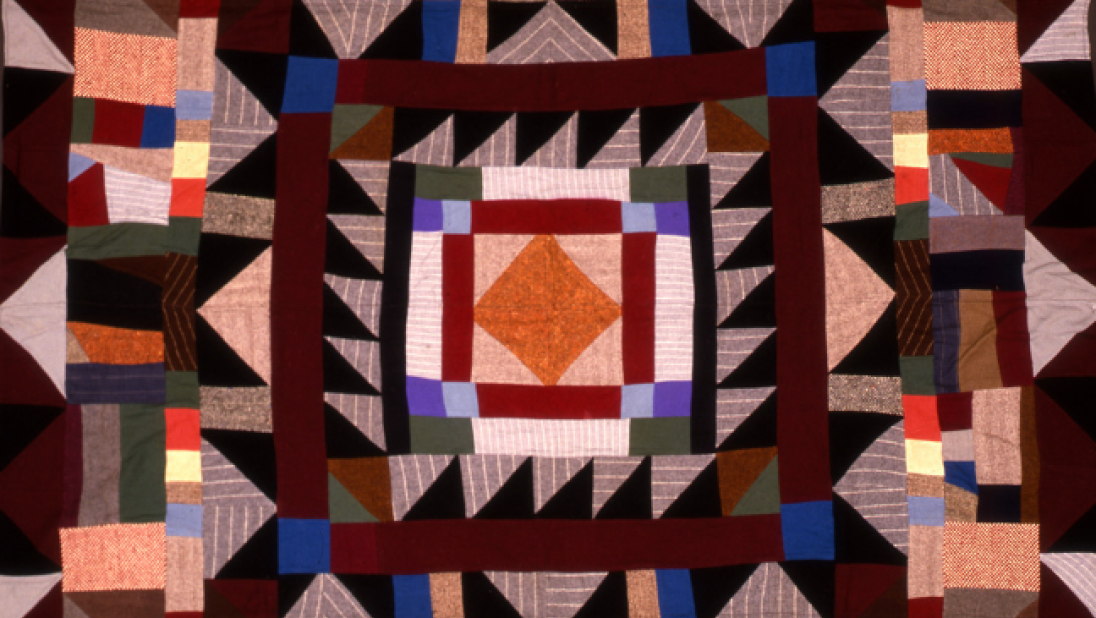 A wildly patterned quilt surrounding an orange diamond centre.