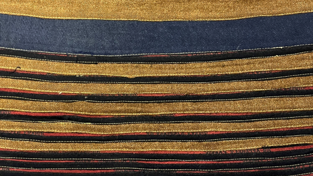 The detail of the back of a rug. It is a striped rug with multiple colours.