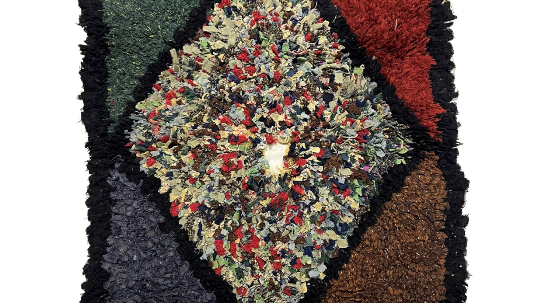 A rectangular rug. The inner shape is multicoloured diamond with a hole inthe middle. It has a black trim.