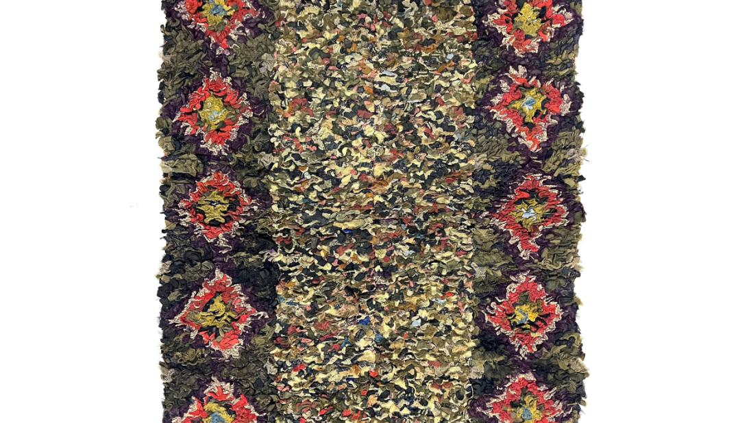 A rectangular rug. The inner part of the rug is a multi-coloured rectangle. The outer rectangle is blue with colourful diamond shaped decorations.