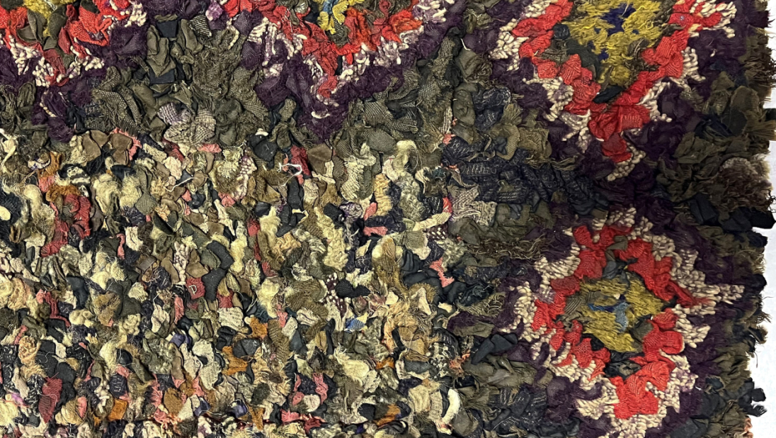A detailed corner of a rug. The inner rectangle is multicoloured. The outer rectangle has multicoloured diamond shapes decorating the rug every few inches.