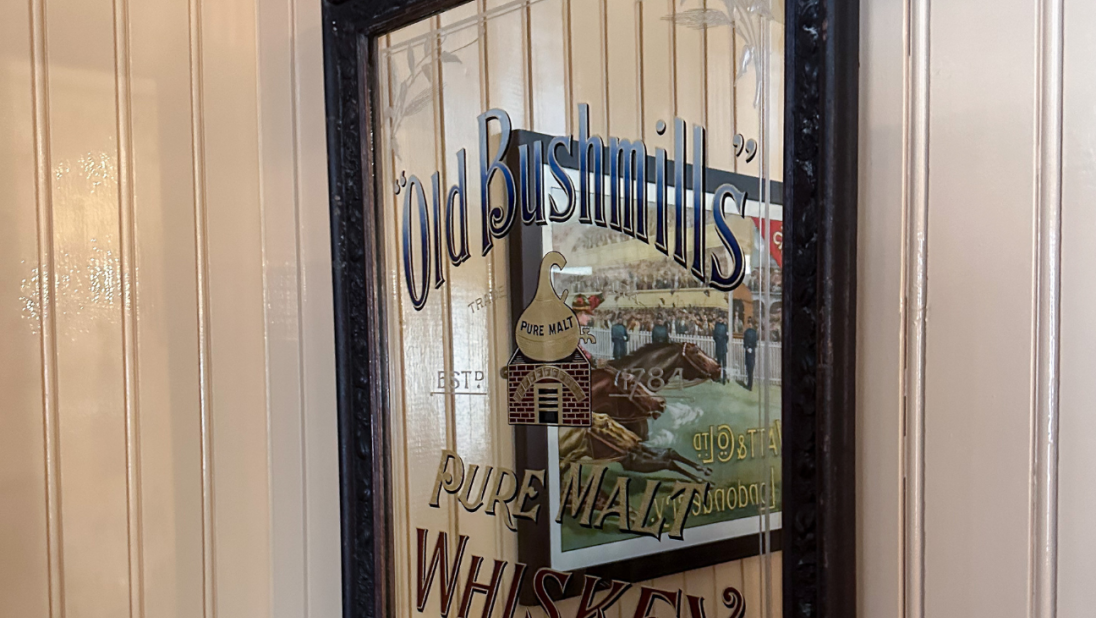 A mirror with a hand-painted advertisment. It reads 'Old Bushmills' Pure Stout Whiskey'.