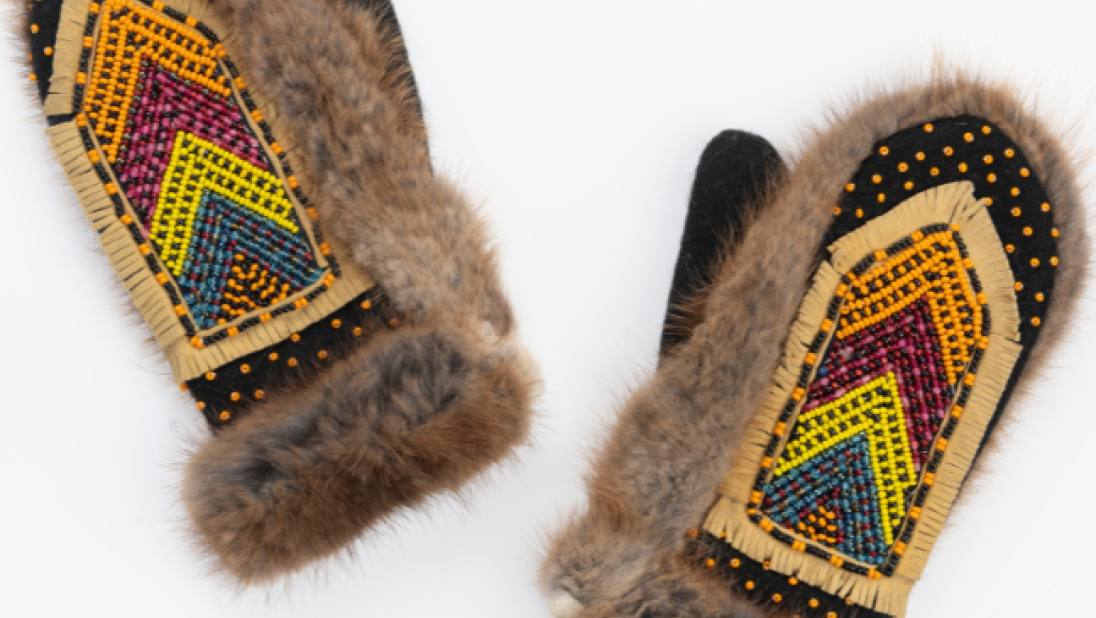 A pair of fur gloves with beading on the back of the hands. The beads are in a v shape pattern and layered by colour, from bottom to top: green, yellow, red, and orange.