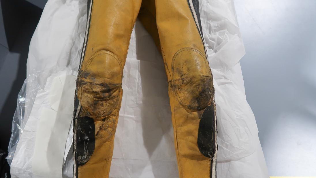 The legs of a yellow and black jumpsuit. The kneepads have undergone conservation and look cleaner than they did in the picture above.