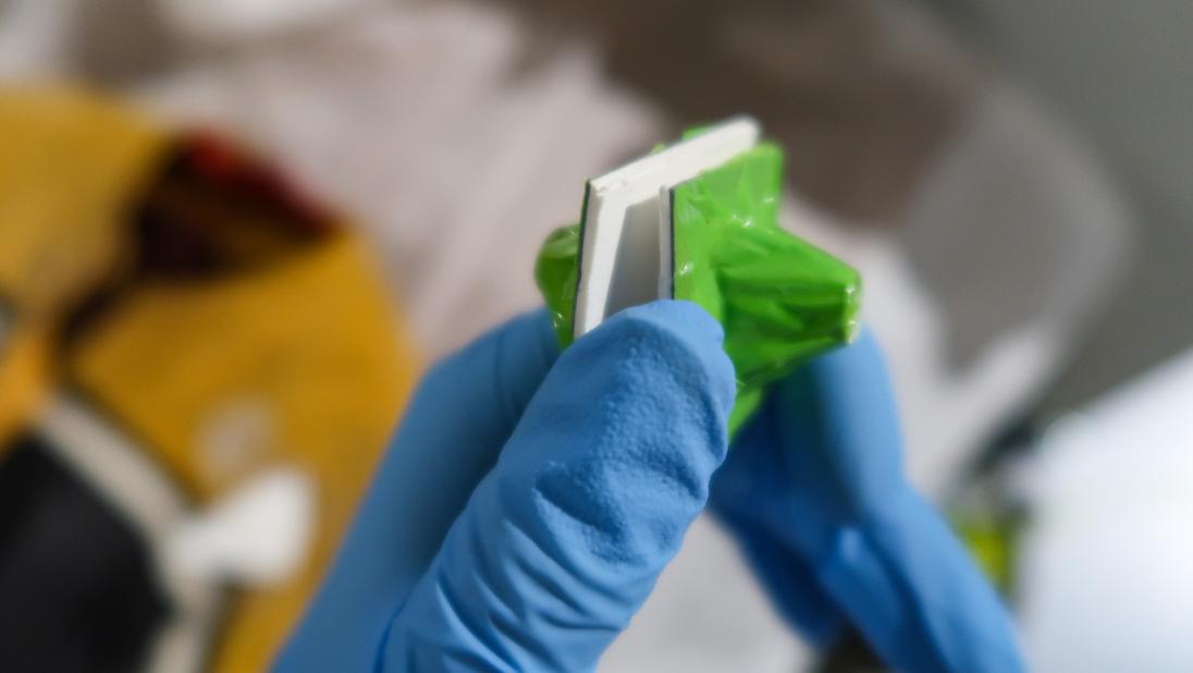 A hand with a blue glove on holds up two small magnets. 