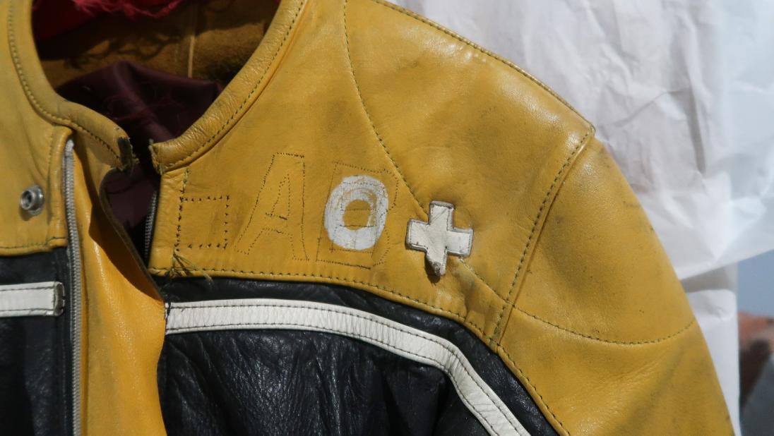 A close up of the top of a racing jumpsuit. There are white patches spelling 'O +' sewn on.