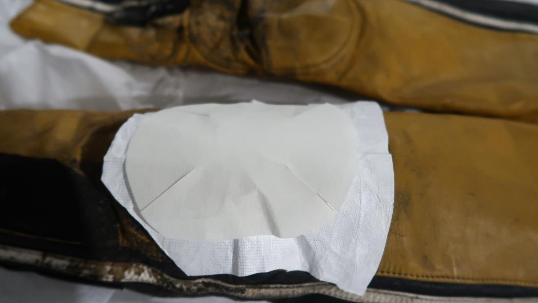 A close up of the knee of a yellow and black jumpsuit with a piece of white cloth over it. Over the cloth is a smaller piece of white cloth.