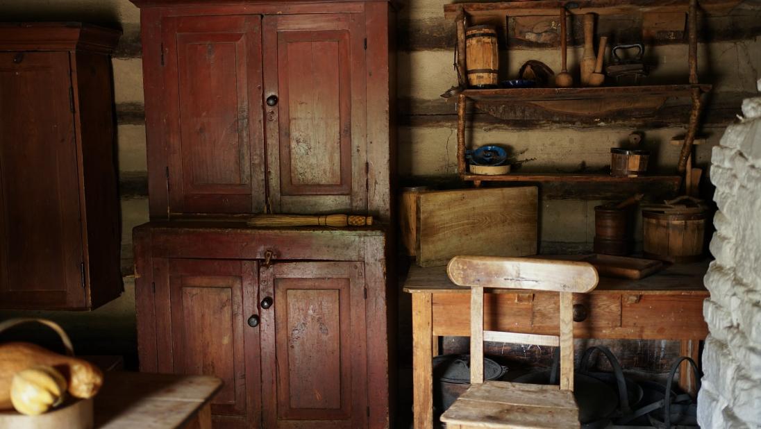 A view inside a log cabin, with a table and sideboard on the left, and a chair and fireplace to the right.