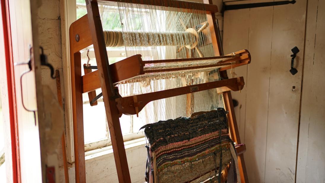 A loom stands at a window. A half finshed blanket is still being woven.