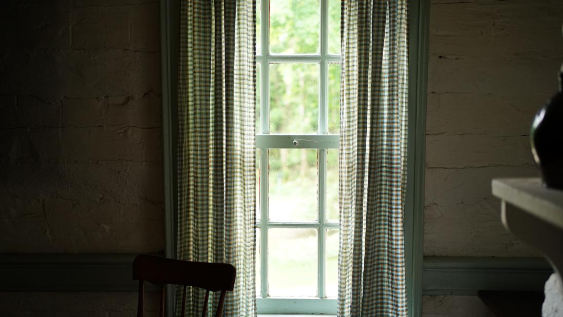 The view out of a window at a log farmhouse, showing a garden and green trees.