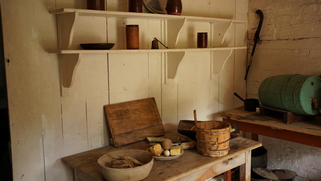 The kitchen of a log farmhouse, showing shelves and a side table.