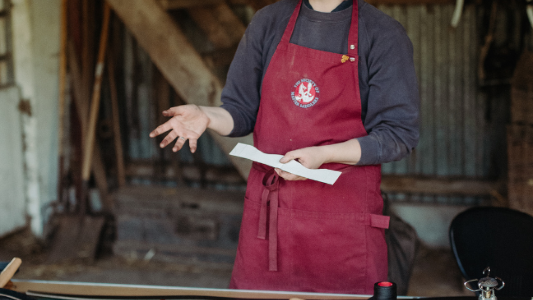 a red haired woman working with leather in a red apron 