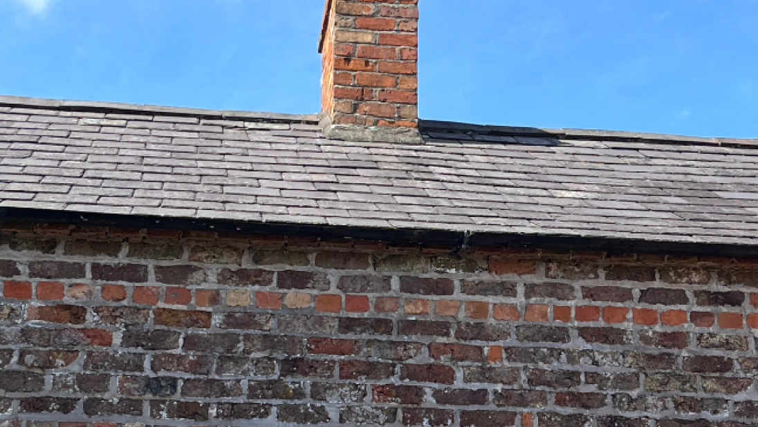 The roof of a vernacular building, where a brick chimney stands restored.