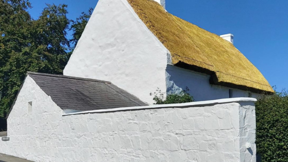 A thatched and whitewashed cottage after a new coat of whitewash stands brightly in the sun.