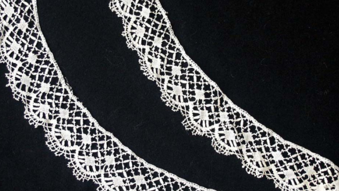 A trim of bobbin lace. The pattern uses diamond shapes, with loops of lace at the edges. 