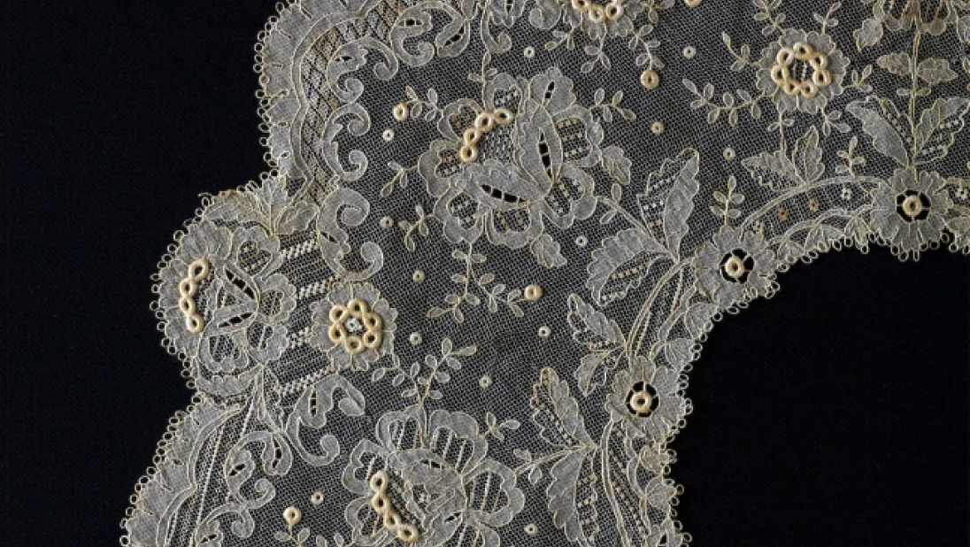 A close up of an intricate lace collar wtih many small floral designs.