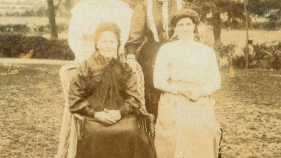 An old black and white photograph of four women posing for a photograph in a garden. Their dress suggests this photograph is from the early 1900s.