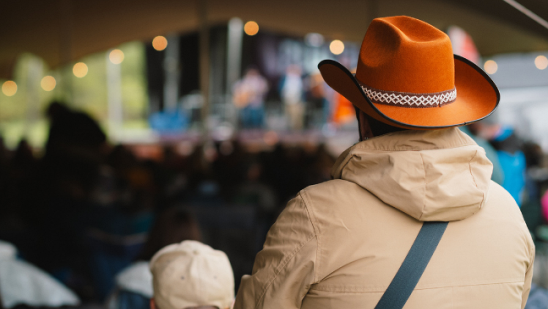 A person in an orange cowboy hat watching music 