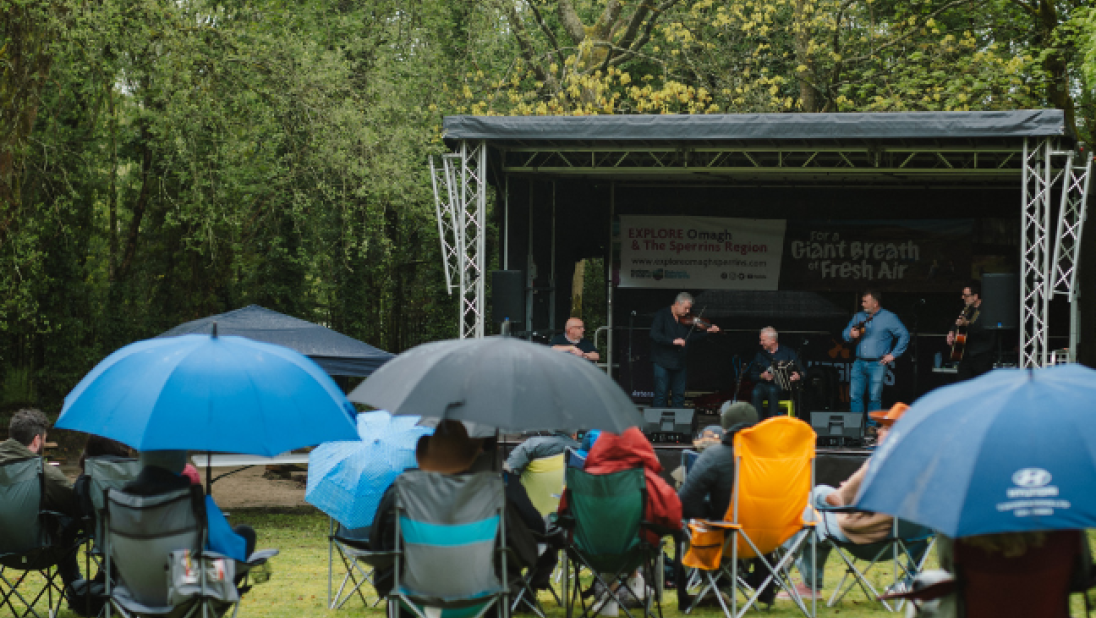 A crowd of people watching a stage in the rain with umbrellas up 