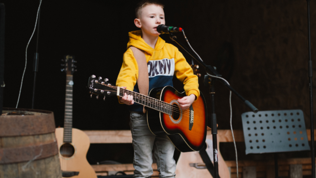 A child in a yellow jumper dinging at an open mic 