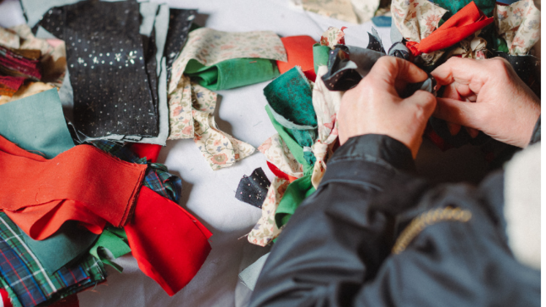 hands creating a red and green rag wreath