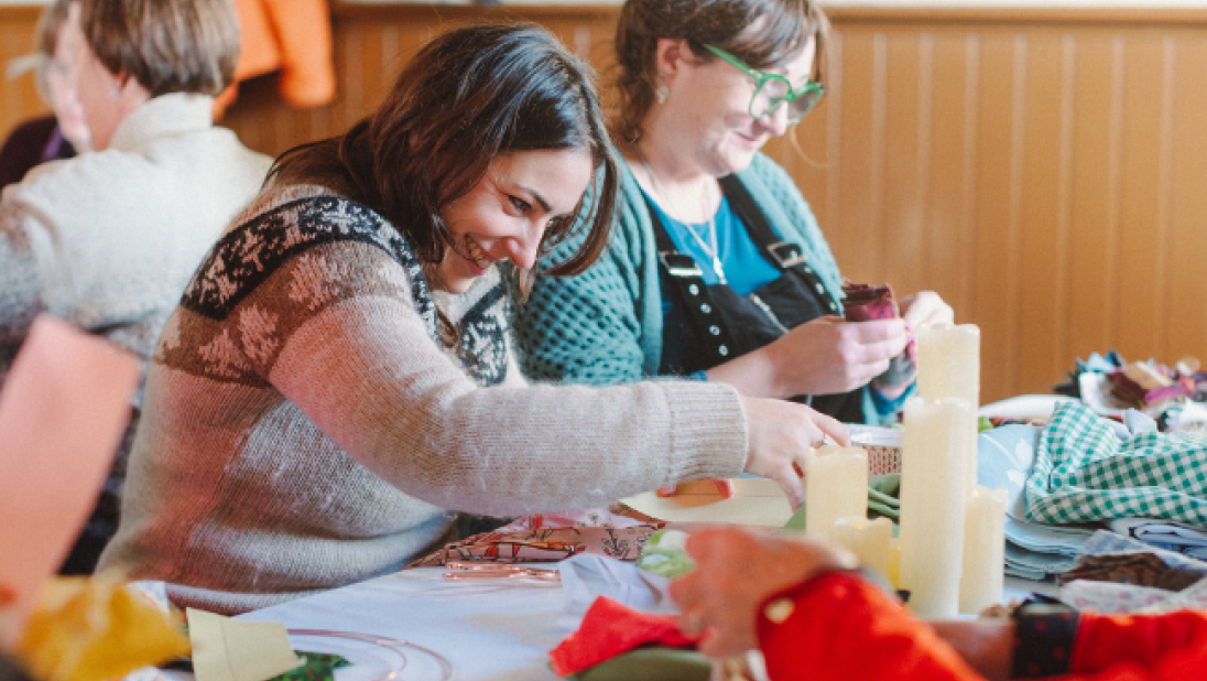 two women smiling while making a rag wreath