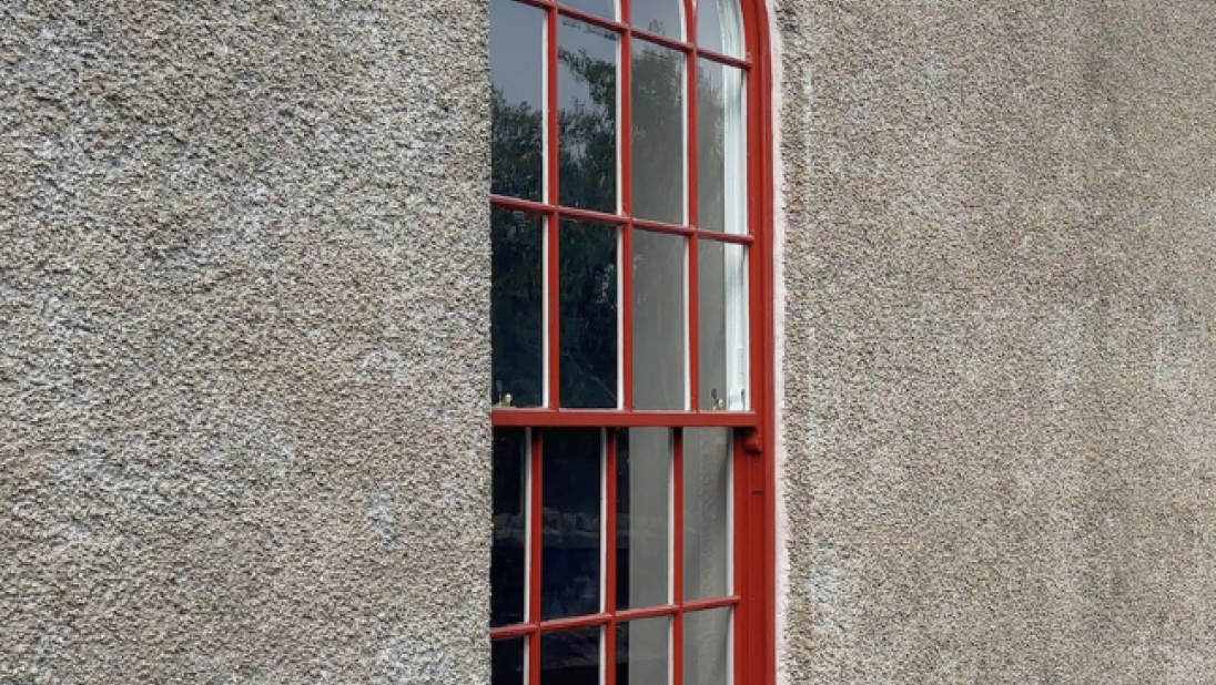 A photograph of a new replica window with bright red trimmings installed in a stone wall.